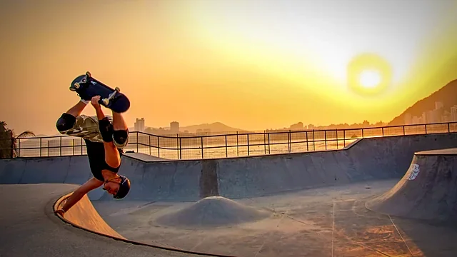 Skateboarder upside down at the lip of a skate bowl at sunset