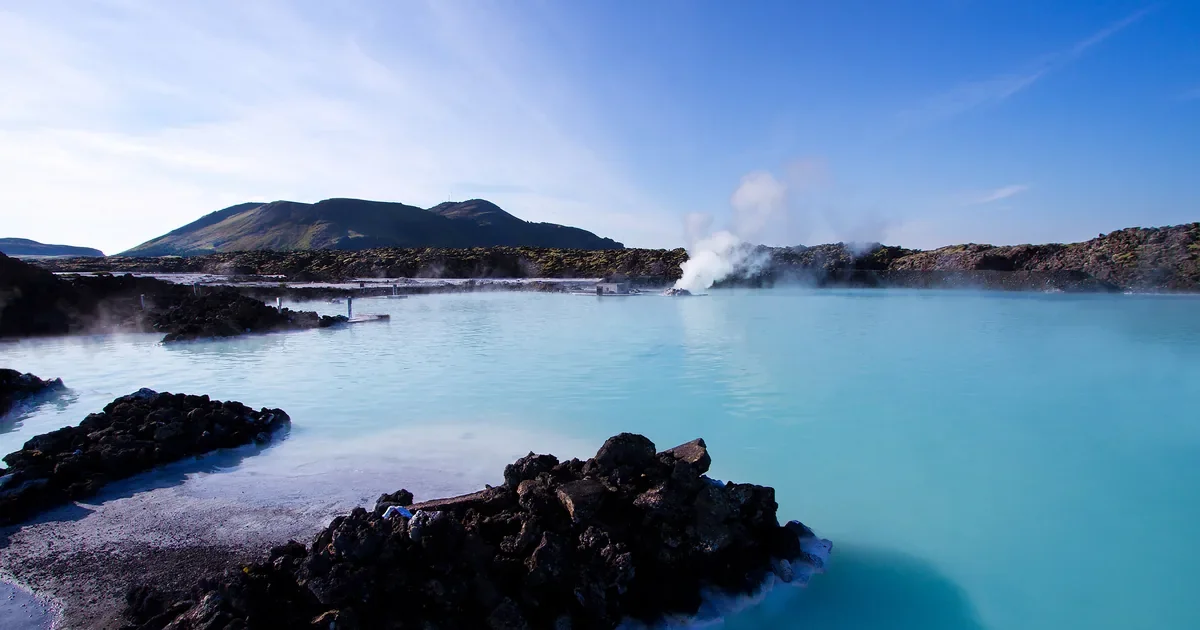 Milky blue geothermal lagoon ringed by dark lava rock under a clear sky