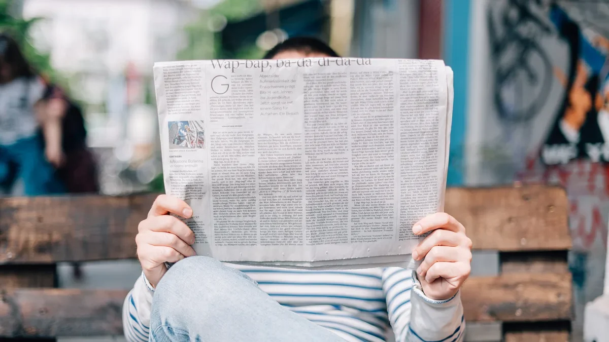 Reader on a bench holding up an open newspaper