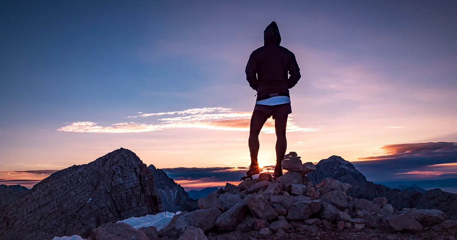 Hiker in a hoodie on rocky high ground at sunset