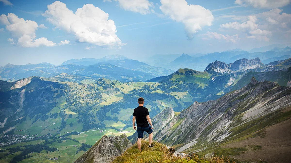Hiker crossing green hills under a cloudy mountain sky