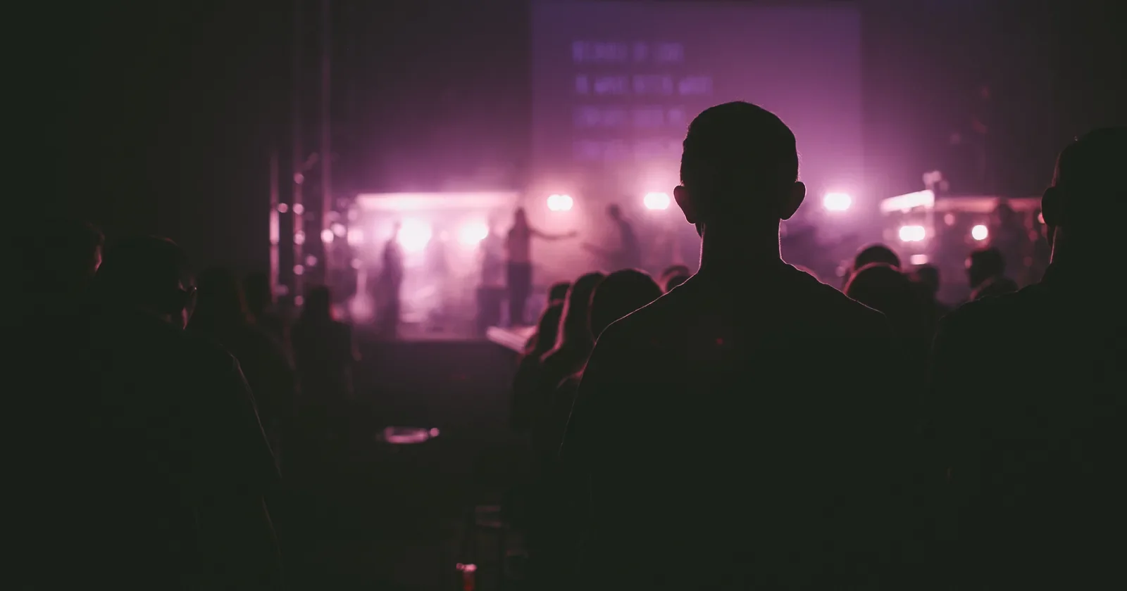 Concert crowd in silhouette watching a stage lit in purple light