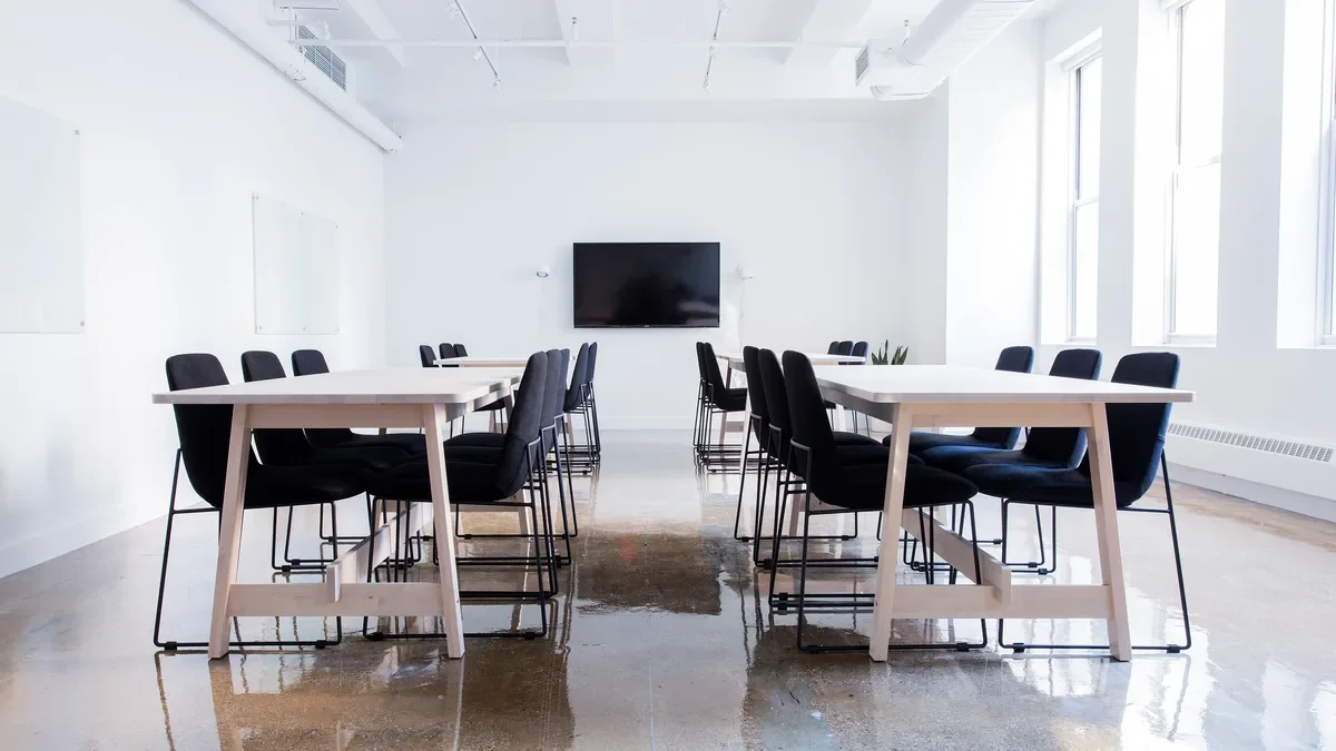 Empty meeting room with two long tables, black chairs and a wall screen