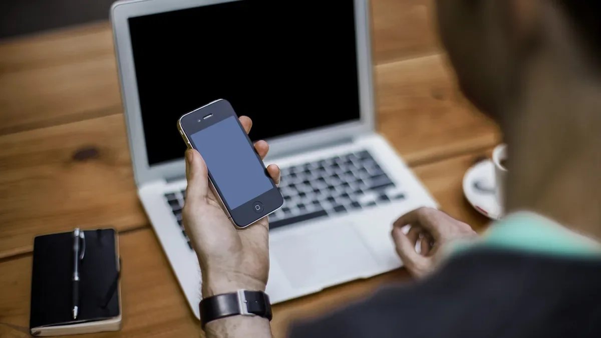 Checking a smartphone next to an open laptop on a wooden desk