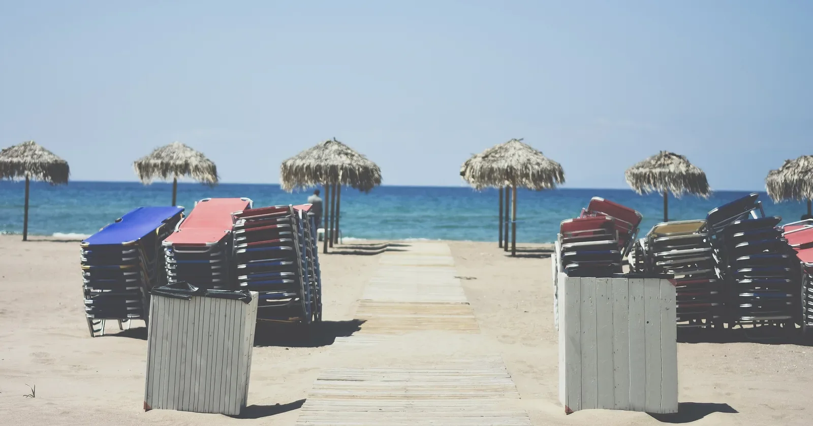 Stacked sun loungers and thatched umbrellas on a sunny sand beach by the sea