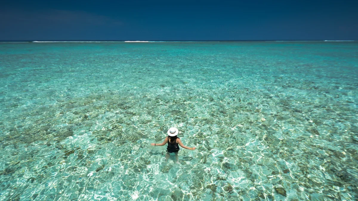 Swimmer in a white hat wading into clear turquoise water