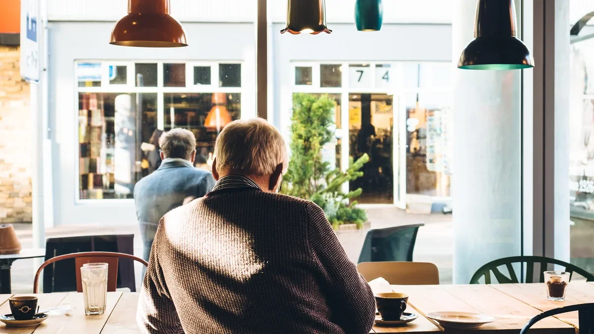 Older reader seen from behind with a cup of coffee at a cafe window