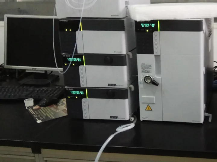 HPLC system with stacked pump, detector and column oven modules beside a data workstation monitor on an analytical laboratory bench